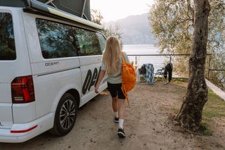 Geheimtipp Urlaub April: Junge Frau in Wanderkleidung neben ihrem Camper auf dem Campingplatz am Meer in Italien