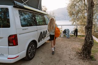 Frau läuft auf Camper zu mit Gardasee im Hintergrund