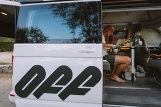 Ein junger Mann kocht in seinem Off Camper auf dem Campingplatz an einer der Spielstätten der EM 2024