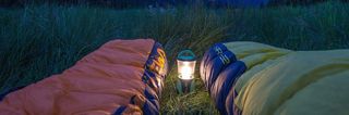 Zwei Schlafsäcke auf einer Wiese mit Outdoor Camping Lampe.