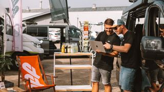 Zwei Männer schauen bei einem event zum Campingbus kaufen etwas auf dem Laptop nach