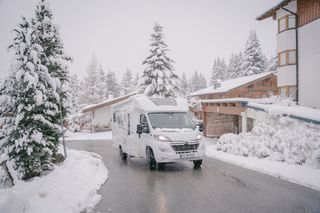 Ein Mooveo Wohnmobil fährt beim Wintercamping eine Straße entlang in verschneiter Umgebung.