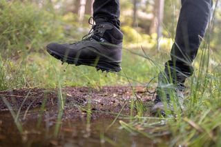 Wanderschuhe im Matsch mit Wald im Hintergrund