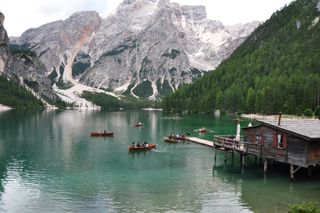 Der Pragser Wildsee gehört zu den Touri Spots in den Dolomiten: Viele Tourist:innen sind auf Booten auf dem See unterwegs, der von Wäldern und Bergen umgeben ist.