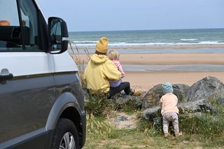 Eine Frau sitzt mit zwei Kindern am Strand.