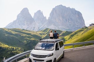 Zwei Menschen sitzen auf dem Dach eines Opel Crosscamp Vans und blicken auf die Landschaft der Dolomiten.