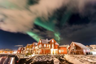 Typisch rote norwegische Holzhäuser bei Nacht und die Polarlichter am Himmel