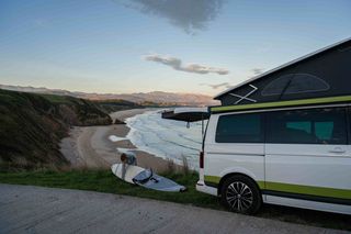 Woman with surfboard on the coast in Portugal next to off camper in winter