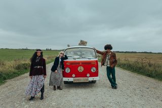 Drei Hippies mit VW Bulli und Peace Schild auf Feldweg