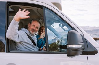 Ein älteres Pärchen winkt aus dem Fenster ihres Off Campers.