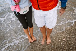 Wo ist es im April warm? Zwei Personen stehen mit den Zehen im Wasser am Strand bei ihrem Urlaub im April in Italien