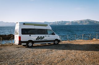 Strom Wohnmobil: Ein Camper mit Off-Schriftzug am Meer auf Mallorca mit einer Bergkette im Hintergrund.