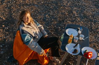 Urlaub mit Sonnenschein im April: Junge Frau schaut mit geschlossenen Augen in die Sonne, während sie am Campingtisch am Strand sitzt