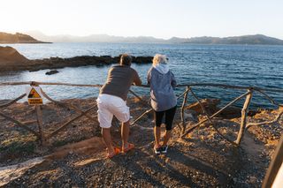 Mallorca als Reiseziel im April: Ein Mann und eine Frau stehen beim Sonnenuntergang mit Blick aufs Meer an der Küste Mallorcas